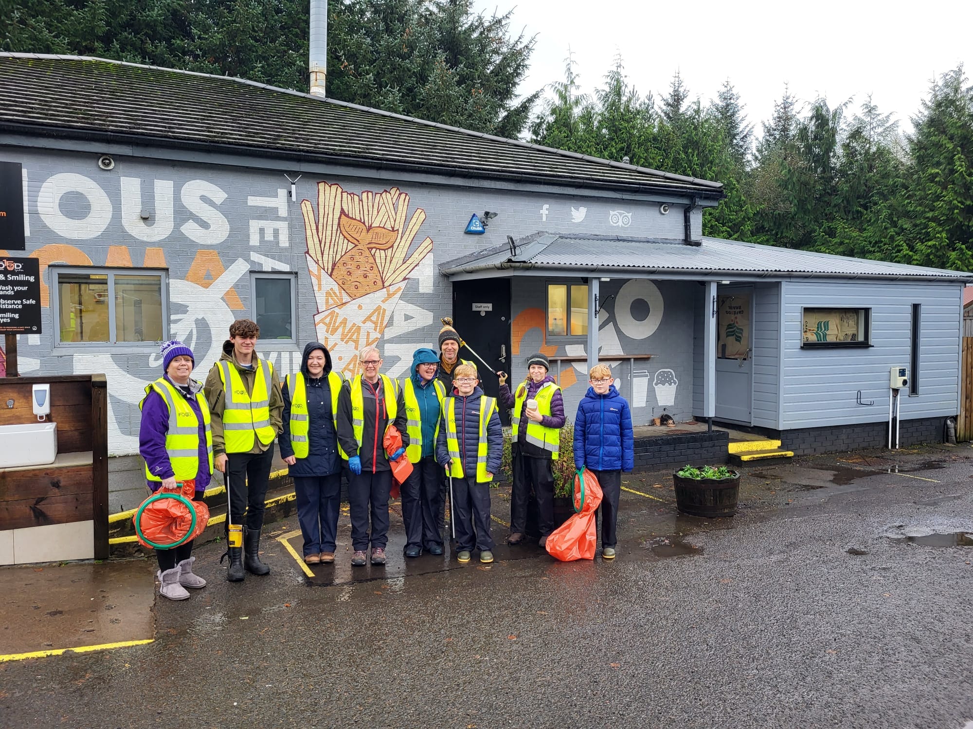 a group of volunteers in high vis vests with litter picking equipment outside The Real Food Cafe in Tyndrum