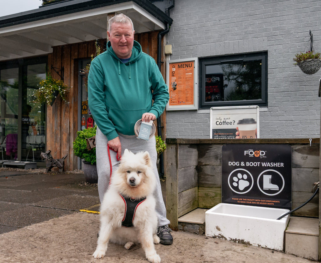 a samoyed dog with his owner standing next to a dog and boot washer in front of a cafe in Tyndrum scotland