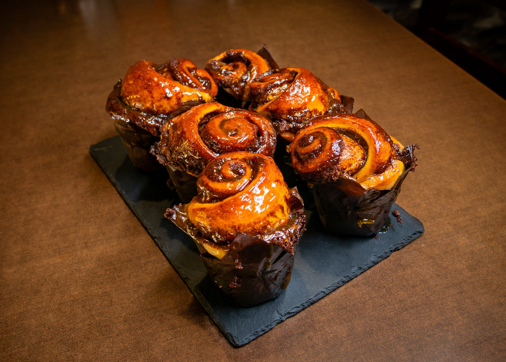 Six glazed shiny cinnamon rolls in muffin paper baskets on a slate plate