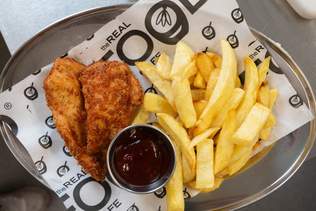 gluten free chicken breast pieces served next to gluten free chips and barbecue sauce on a greseproof branded paper with the real food cafe tyndrum logo