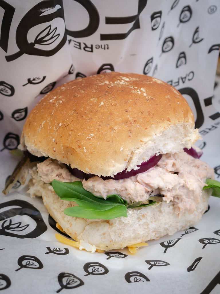 an appetising white roll filled with red onion, tuna mayo and a salad. Wrapped in greased proof paper with The Real Food Cafe logo. 